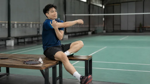 Pemain badminton meregangkan bahu setelah latihan smash