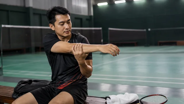 Pemain badminton meregangkan lengan setelah bermain