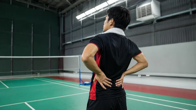 Pemain badminton memegang pinggang setelah bermain